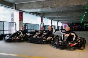 Des amis âgés s'amusent à faire des courses de karts à l'intérieur, faisant preuve d'esprit sportif et d'amitié.
